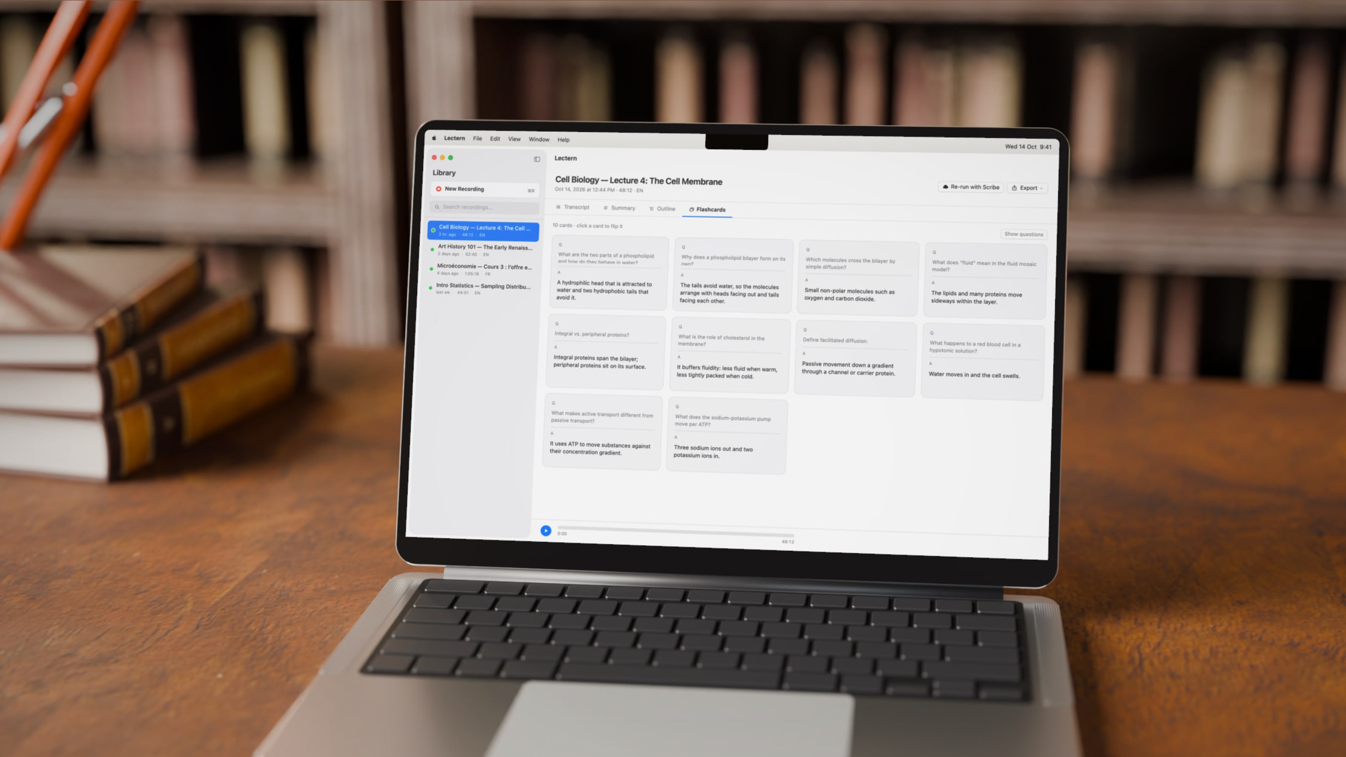 A silver MacBook Pro open on a wooden desk in front of library bookshelves, showing Lectern's Flashcards tab for a Cell Biology lecture with every card flipped to show its answer.